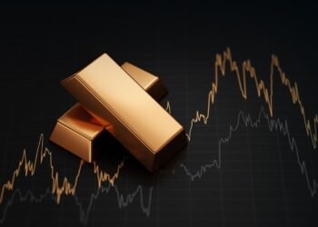 Stack of gold bullion bars and financial market trading screen display